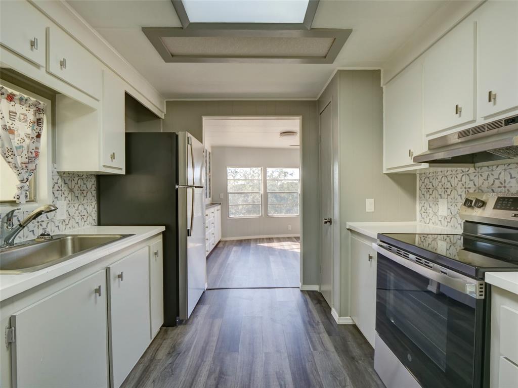 A kitchen with white cabinets, stainless steel appliances, and wood-look flooring leads to a dining area — 2218 ORANGEWOOD CIRCLE UNIT 1540, ZELLWOOD, FL