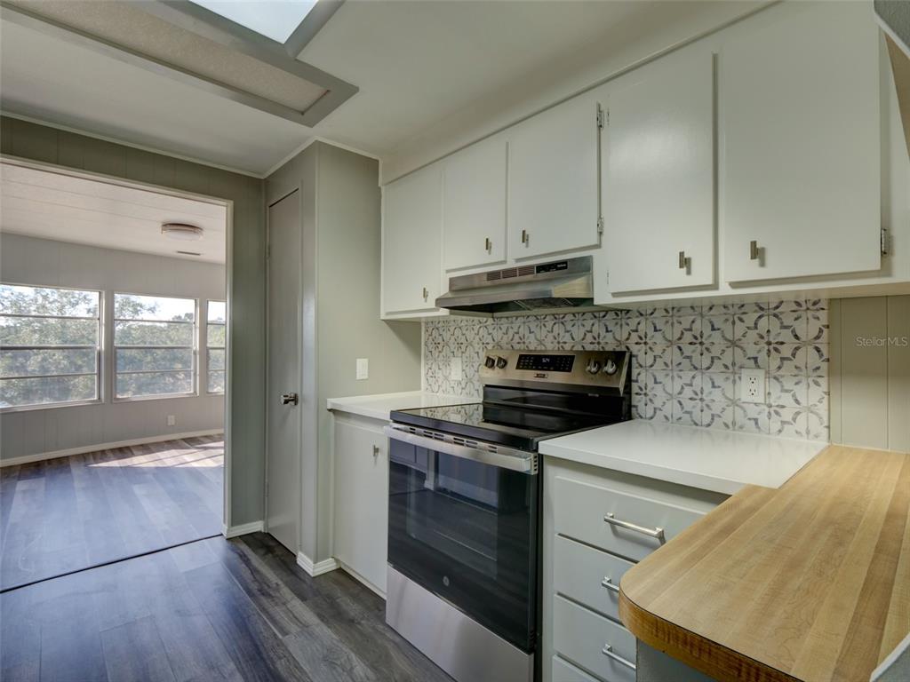 A kitchen features white cabinets, a patterned backsplash, a black stove, and wood-look flooring — 2218 ORANGEWOOD CIRCLE UNIT 1540, ZELLWOOD, FL