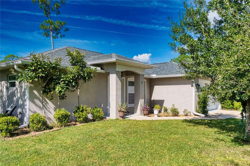 A single-story house with a beige stucco exterior, a gray shingled roof, and landscaped yard — 1 LLOSEE COURT, PALM COAST, FL