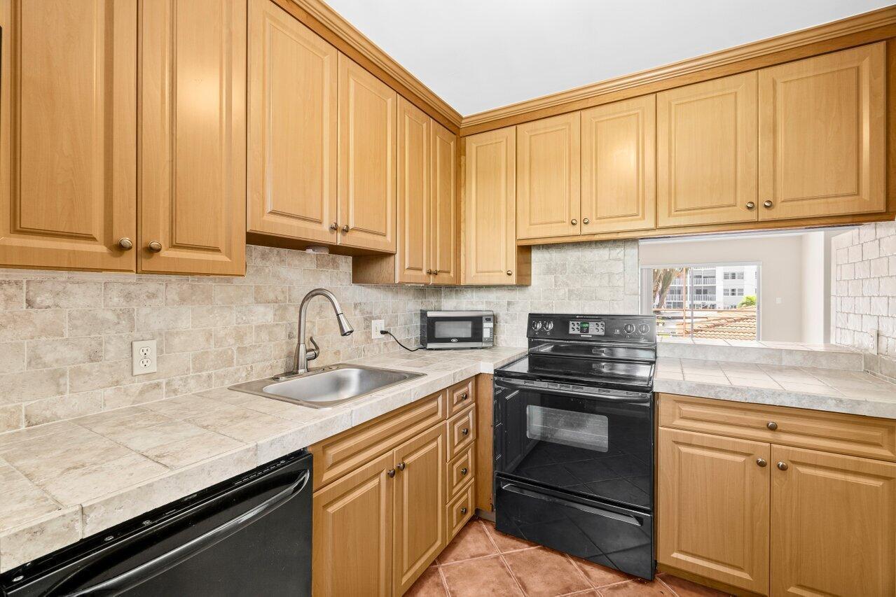 A kitchen with light wood cabinets, tile countertops, a stainless steel sink, and black appliances — 1430 S Lakeside Drive # 22, FL 33460, FL