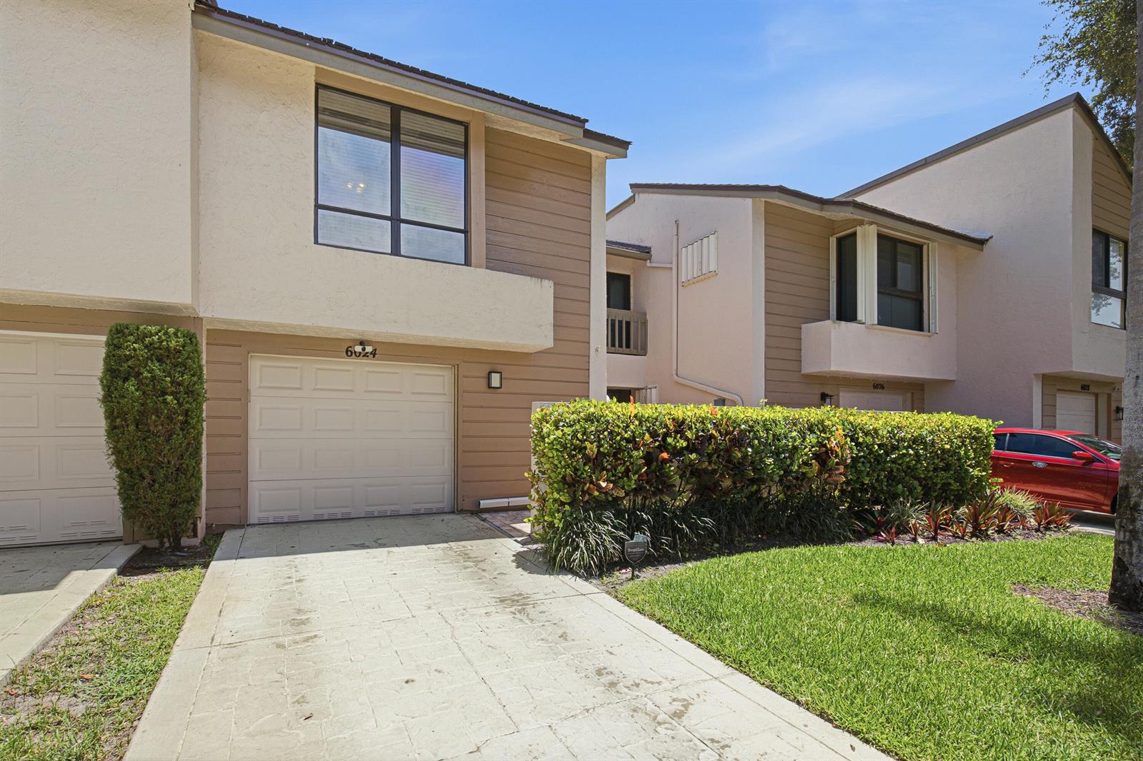 The exterior of a two-story townhouse features a garage, a driveway, and a manicured hedge — 6024 Glendale Drive, Boca Raton FL 33433, BOCA RATON, FL