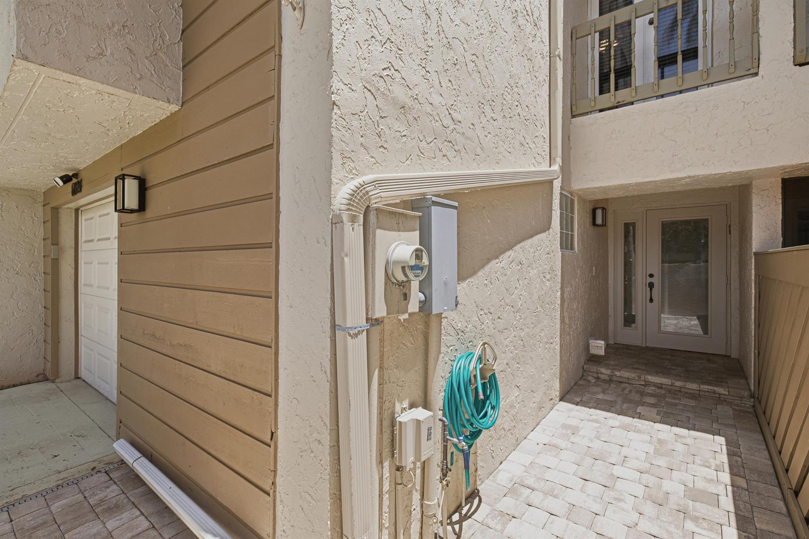 An exterior view of a building entrance with a paved walkway, hose, and utility meters — 6024 Glendale Drive, Boca Raton FL 33433, BOCA RATON, FL