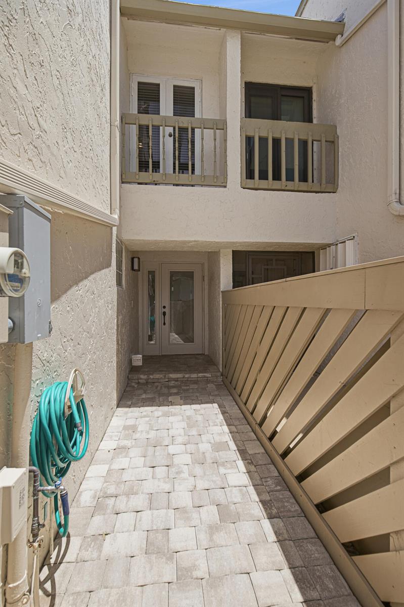 A paved walkway leads to a front entrance with a balcony above and wooden fencing — 6024 Glendale Drive, Boca Raton FL 33433, BOCA RATON, FL