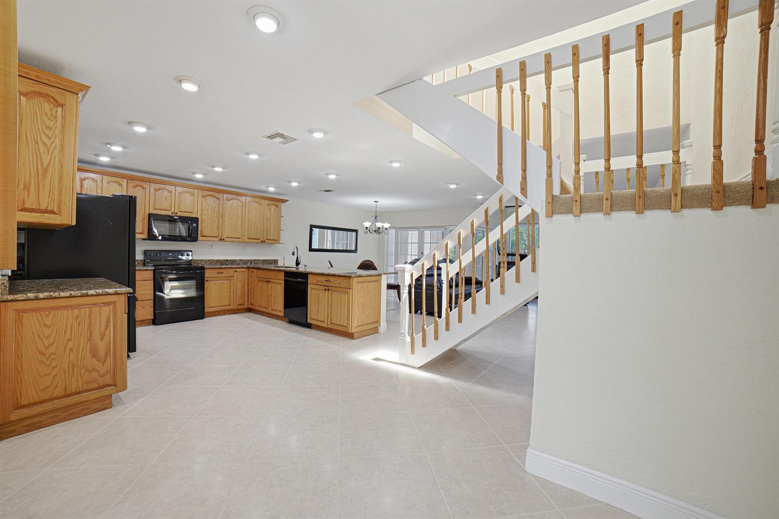 A kitchen with oak cabinets and black appliances sits next to a white staircase — 6024 Glendale Drive, Boca Raton FL 33433, BOCA RATON, FL