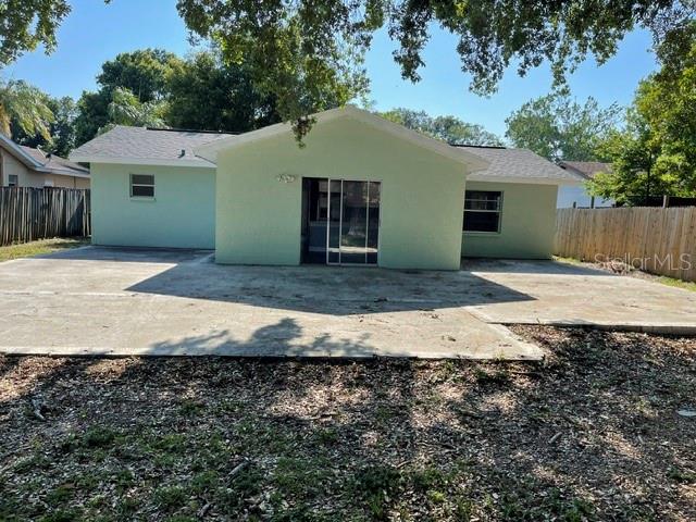The back exterior of a light green house features a concrete patio and sliding glass doors — 2055 DODGE STREET, CLEARWATER, FL