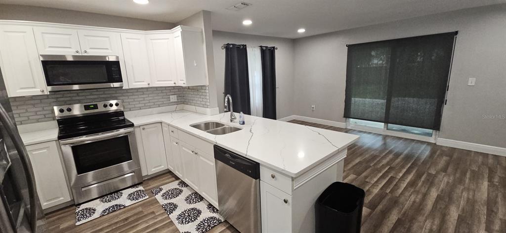 A kitchen features white cabinets, stainless steel appliances, a quartz island, and wood-look flooring — 2055 DODGE STREET, CLEARWATER, FL
