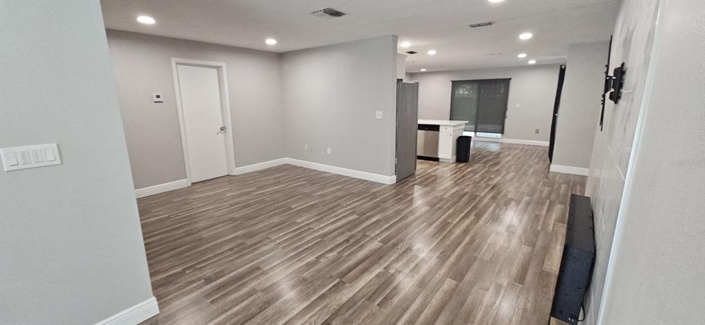 An open-concept living area features light gray walls, wood-look flooring, and a kitchen in the background — 2055 DODGE STREET, CLEARWATER, FL