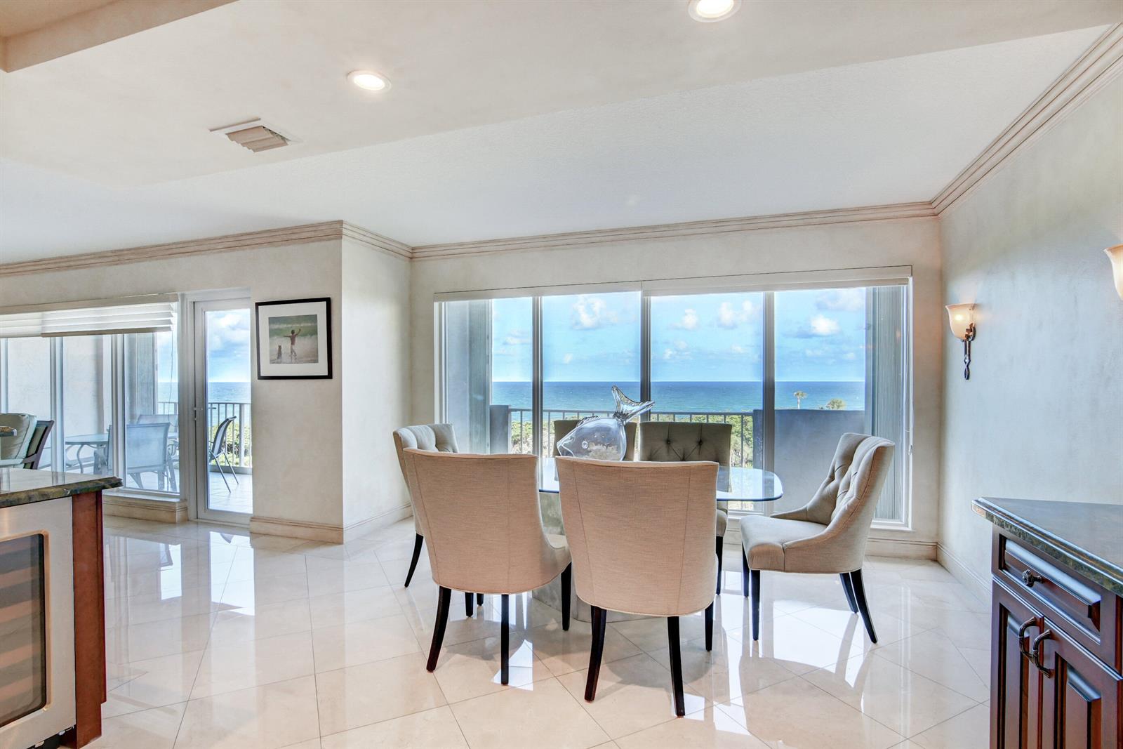 A dining area with a glass table and chairs overlooks the ocean through large windows — 4301 N Ocean Boulevard # 607, Boca Raton FL 33431, BOCA RATON, FL