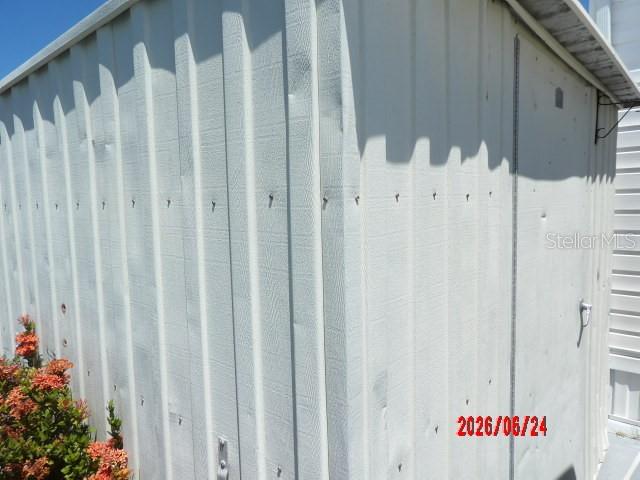 A white metal storage shed stands outdoors next to a flowering bush — 1475 FLAMINGO DRIVE UNIT 105, ENGLEWOOD, FL