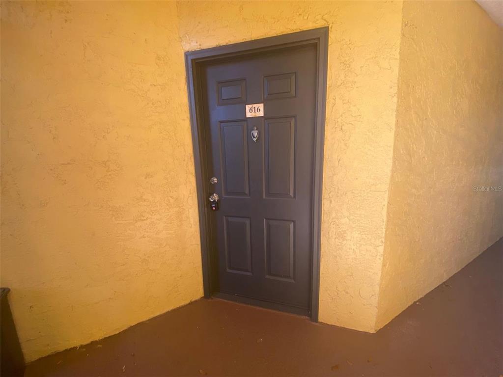A dark gray apartment door labeled 616 is set into a textured yellow wall — 5773 GATLIN AVENUE UNIT 616, ORLANDO, FL