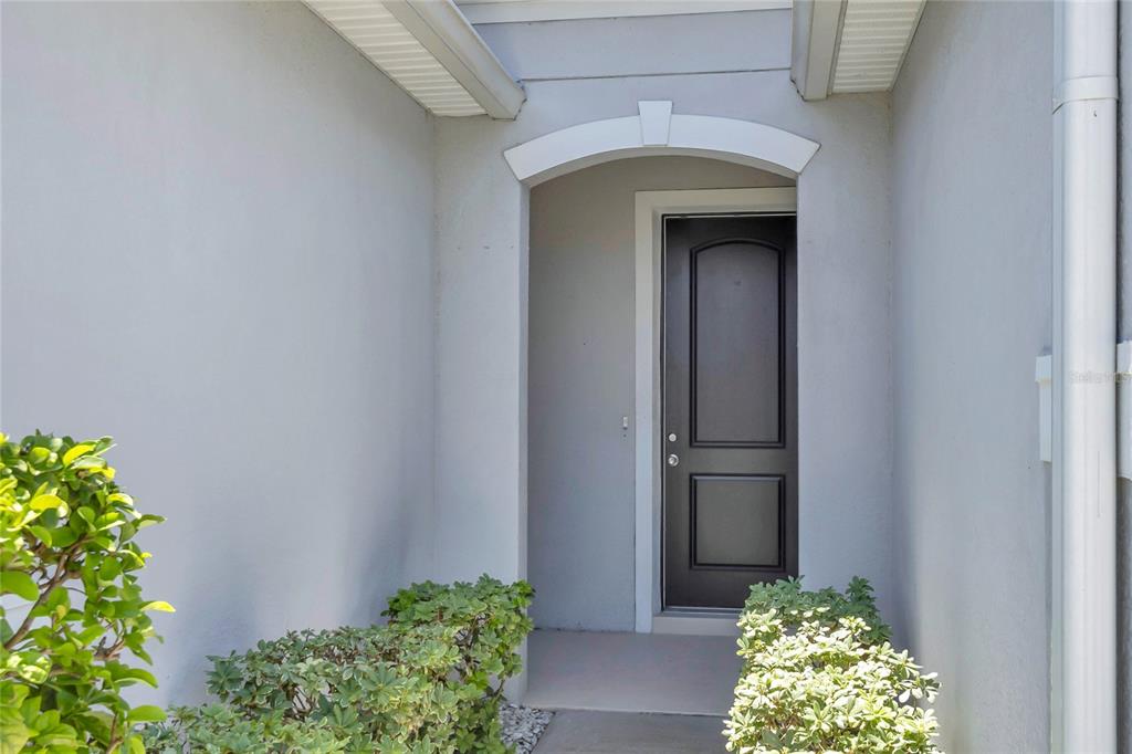 A dark front door is recessed within a light-colored exterior entryway with landscaping — 14571 WARD ROAD, ORLANDO, FL
