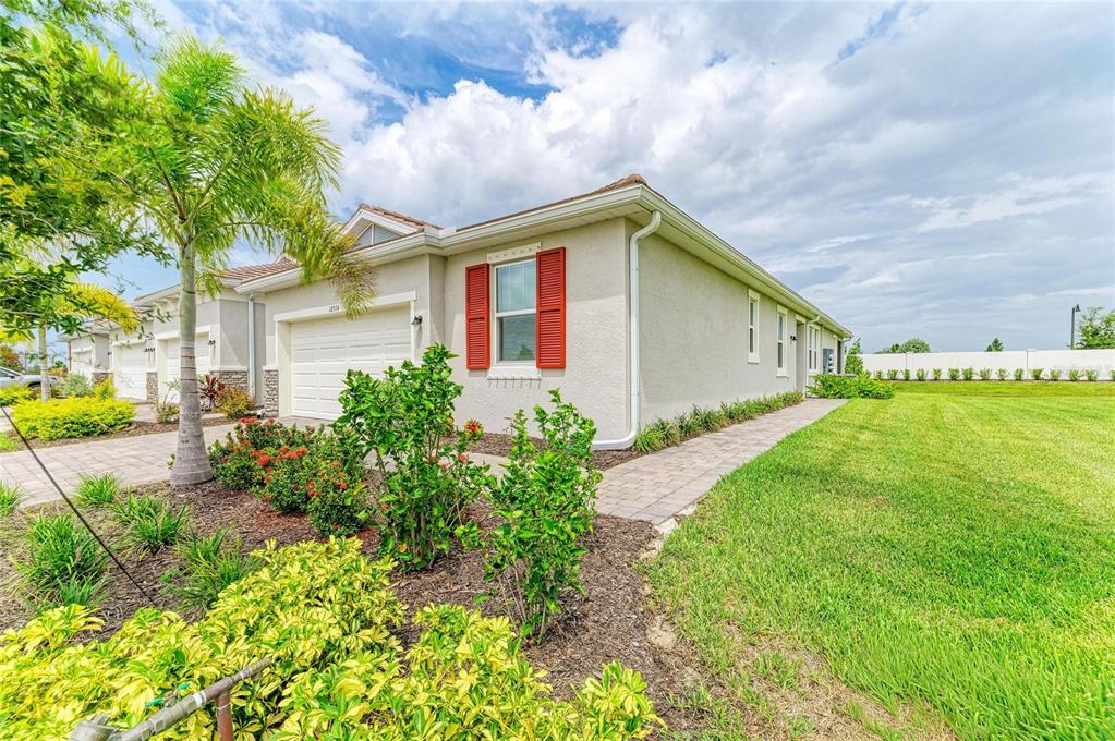 A side view of a beige house with red shutters, a paver walkway, and landscaping — 12574 SOMATIC COURT, VENICE, FL