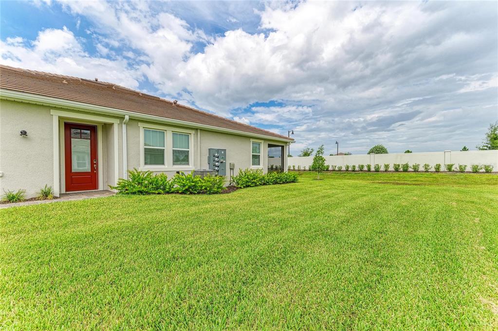 A side view of a house exterior featuring a red door, lawn, and privacy wall — 12574 SOMATIC COURT, VENICE, FL