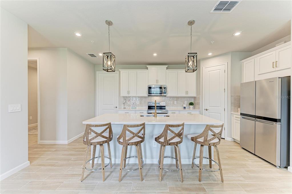 A kitchen features white cabinetry, a central island with four wooden stools, and stainless appliances — 12574 SOMATIC COURT, VENICE, FL