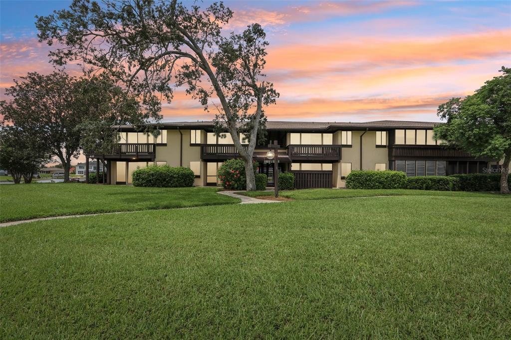 A two-story apartment building with a large tree and lawn in the foreground — 46 CLUB HOUSE DRIVE UNIT 108, PALM COAST, FL