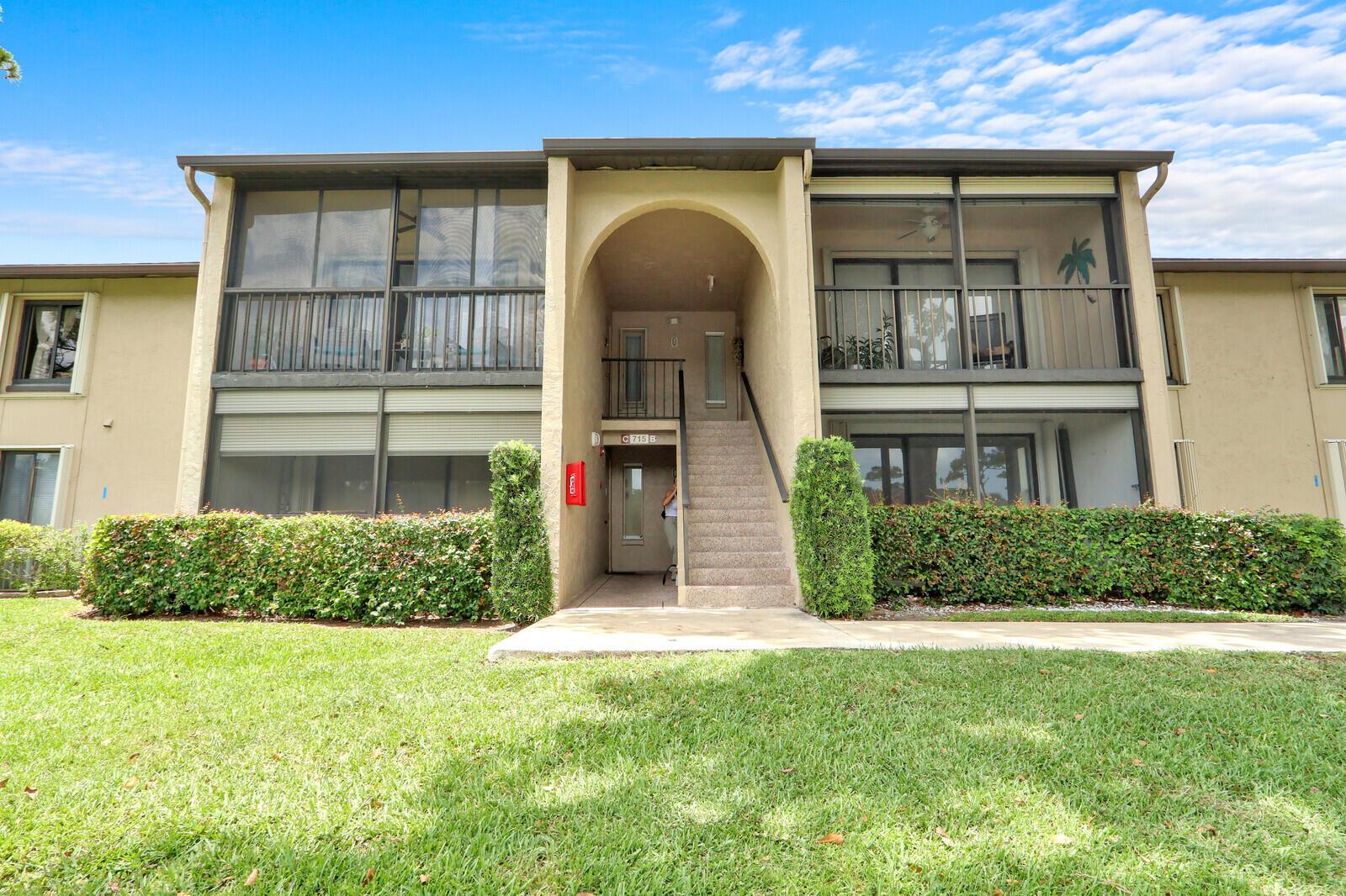 A two-story apartment building exterior features screened balconies, a central staircase, and manicured hedges — 715 Sunny Pine Way # B1, FL 33415, FL