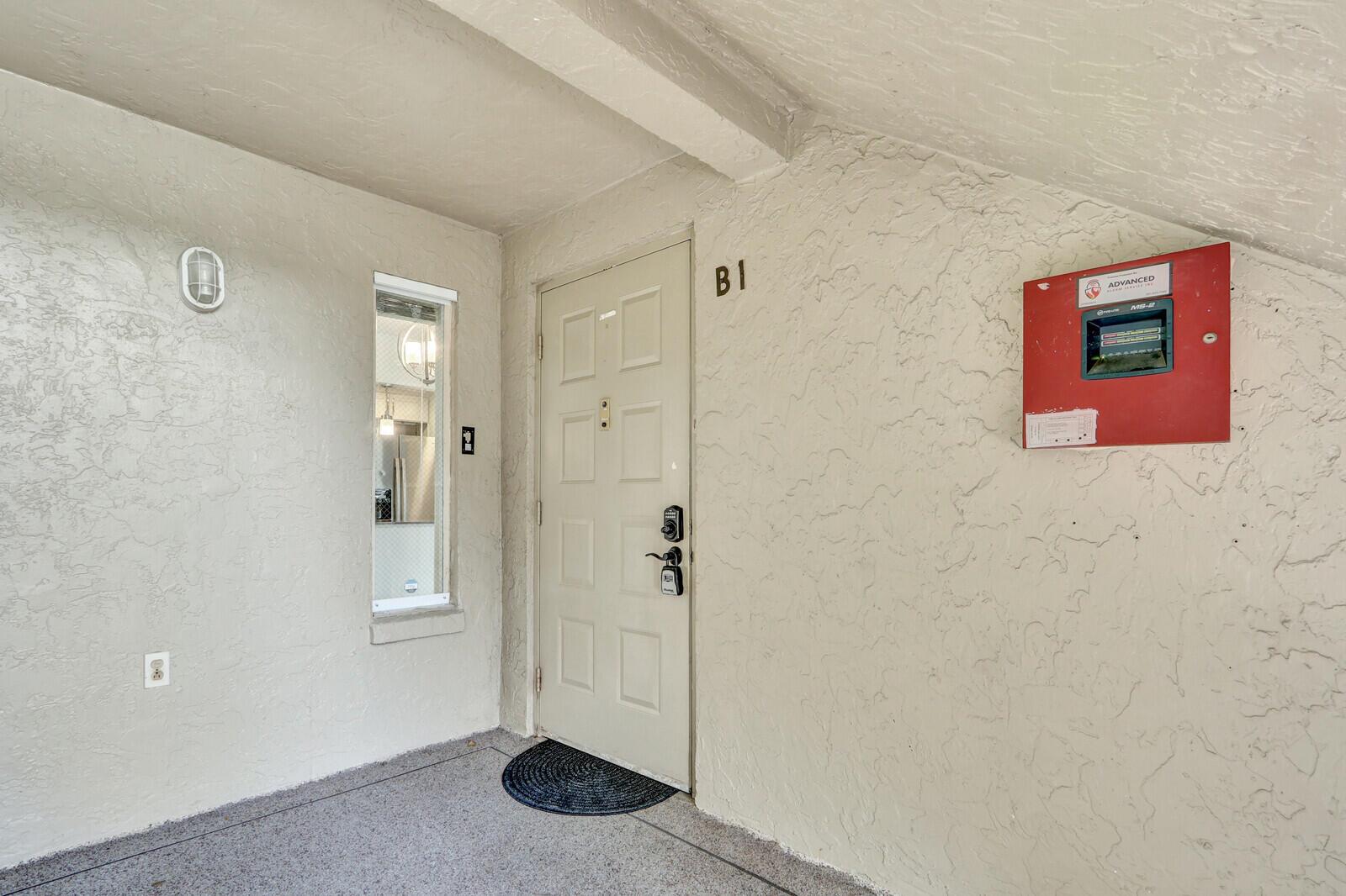 An exterior view of a residential entrance door labeled B1 with a red alarm panel — 715 Sunny Pine Way # B1, FL 33415, FL