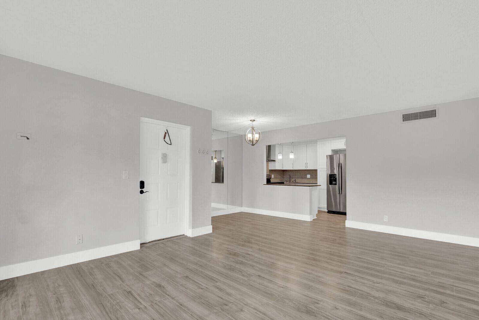 An open-concept living area with light wood-look flooring, gray walls, and a white kitchen — 715 Sunny Pine Way # B1, FL 33415, FL