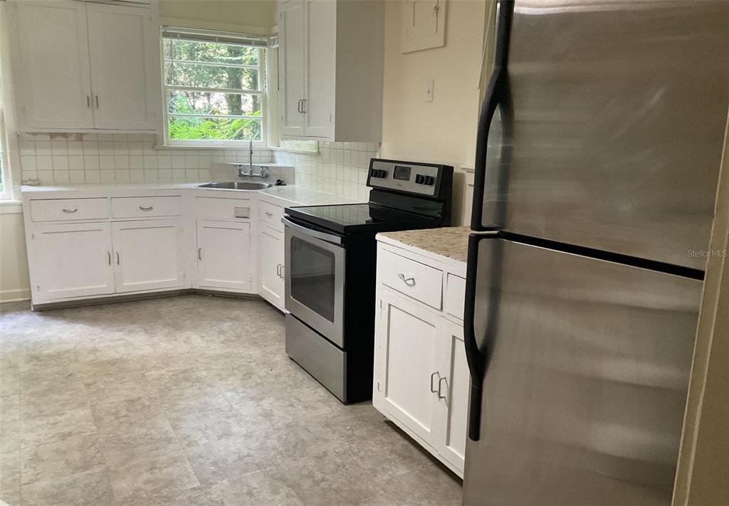 A kitchen features white cabinets, a stainless steel refrigerator, a black stove, and tile flooring — 2721 SW 3RD PLACE, GAINESVILLE, FL
