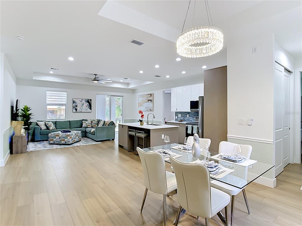 An open-concept living and dining area features light wood flooring, white cabinetry, and a chandelier — 4586 MAURBACH TERRACE, NORTH PORT, FL