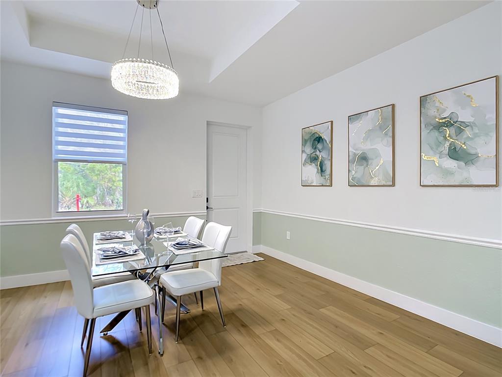 A dining room features a glass table, white chairs, sage wainscoting, and three abstract paintings — 4586 MAURBACH TERRACE, NORTH PORT, FL