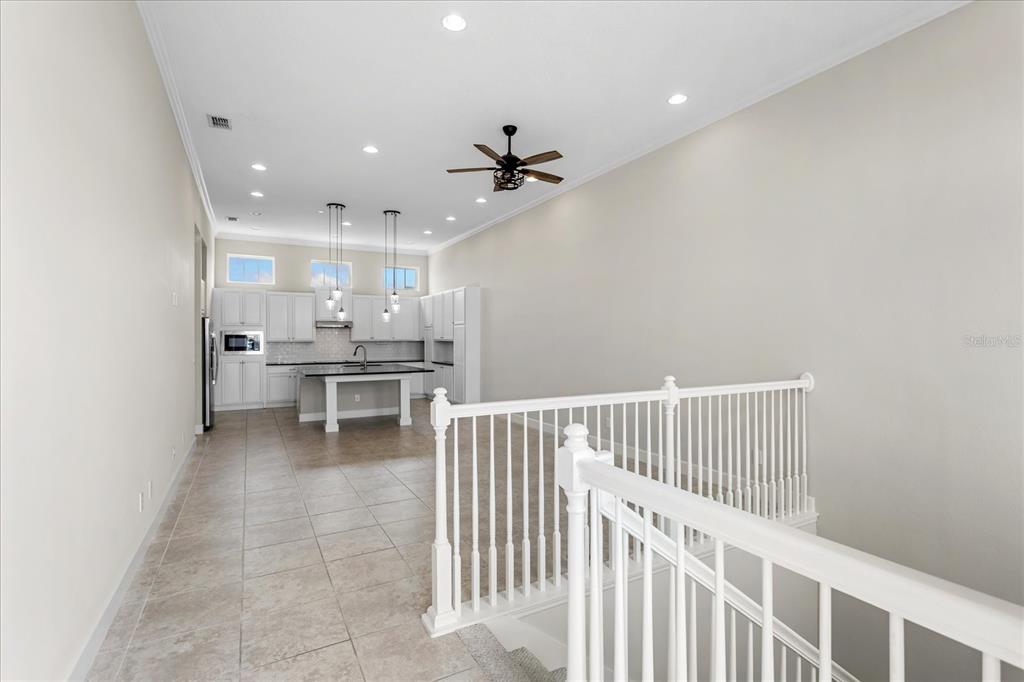 A kitchen with white cabinets and a central island overlooks a staircase with railings — 13433 GRANGER AVENUE, ORLANDO, FL