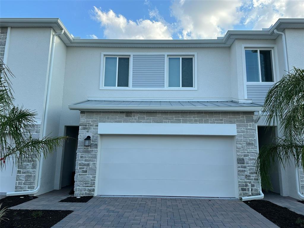 The exterior of a two-story townhouse features a stone facade, a white garage door, and windows — 225 BOGEY DRIVE, DAVENPORT, FL