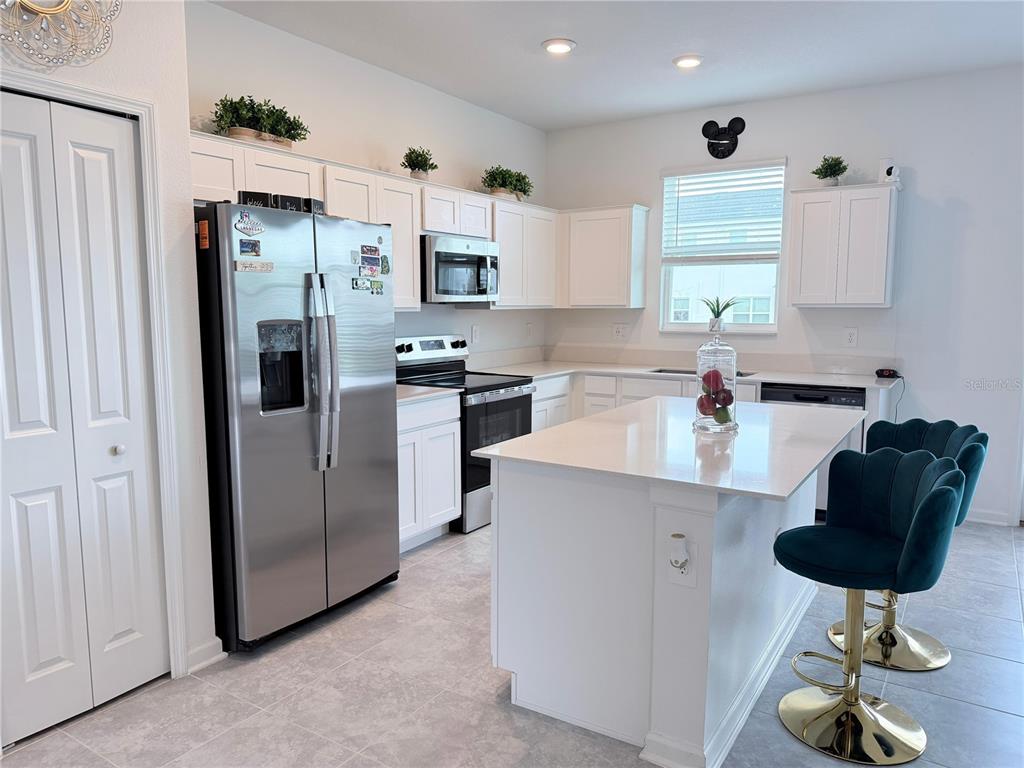 A kitchen features white cabinets, stainless steel appliances, a center island, and teal bar stools — 225 BOGEY DRIVE, DAVENPORT, FL