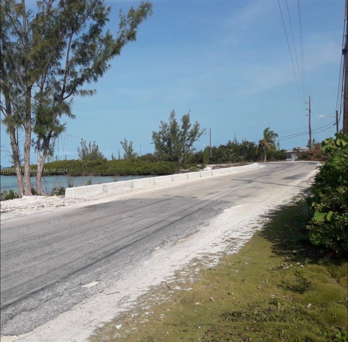 A paved road curves alongside a body of water with a concrete barrier and trees — DOCTORS CREEK JPOSIAH TANTAILS, LONG ISLAND BAHAMAS, NA, NA