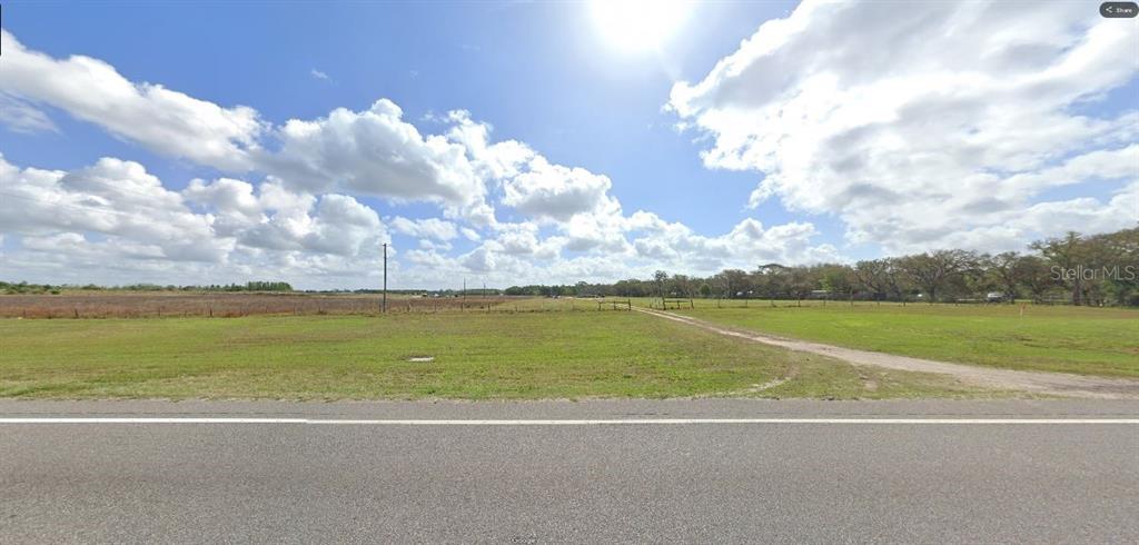 A wide, grassy vacant lot borders a paved road under a bright, cloudy sky — COMMONWEALTH AVE N, POLK CITY, FL