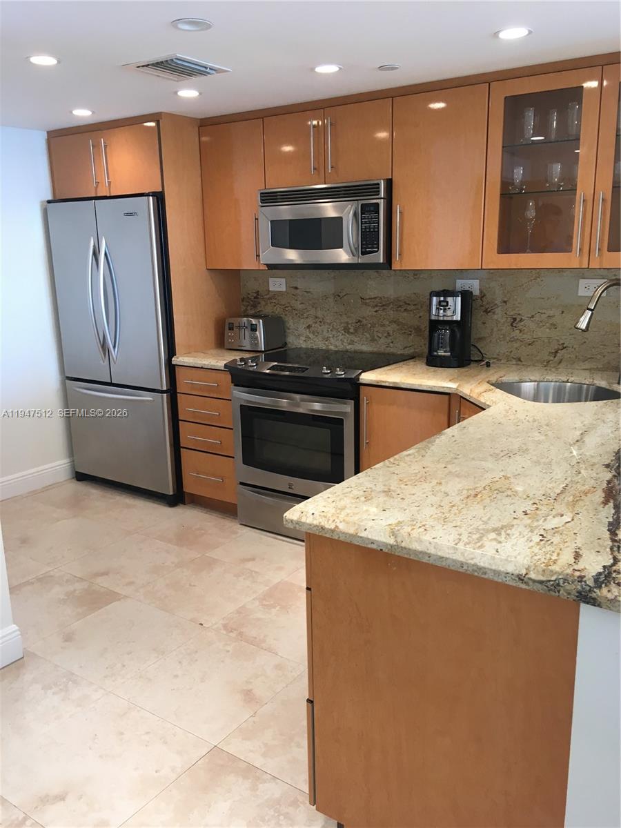 A kitchen features light wood cabinets, stainless steel appliances, and speckled granite countertops — 2625 Collins Ave # 1407, Miami Beach FL 33140, MIAMI BEACH, FL