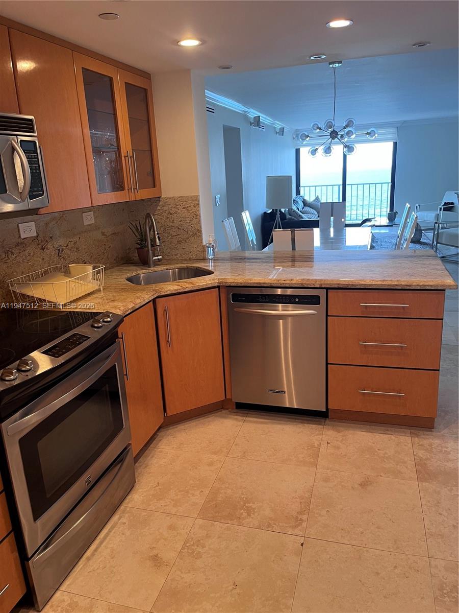 A kitchen with light wood cabinets, granite countertops, and stainless steel appliances overlooks a living area — 2625 Collins Ave # 1407, Miami Beach FL 33140, MIAMI BEACH, FL