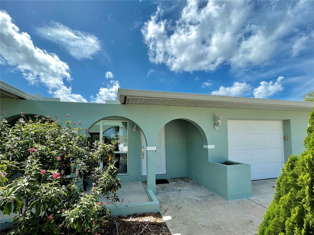 A light green house exterior features an arched entryway, a white garage door, and landscaping — 129 COUSLEY DRIVE SE, PORT CHARLOTTE, FL