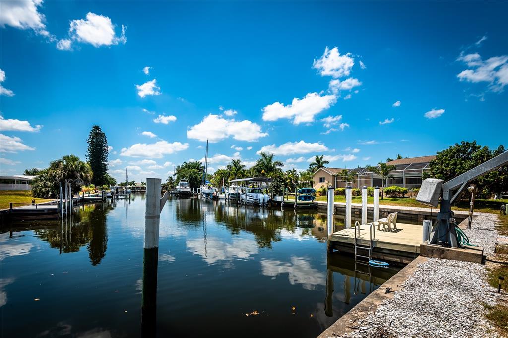 A canal view featuring a wooden boat dock, pilings, and several boats under a blue sky — 129 COUSLEY DRIVE SE, PORT CHARLOTTE, FL