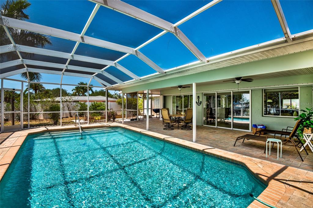 A screened-in swimming pool sits on a patio next to a house with sliding doors — 129 COUSLEY DRIVE SE, PORT CHARLOTTE, FL