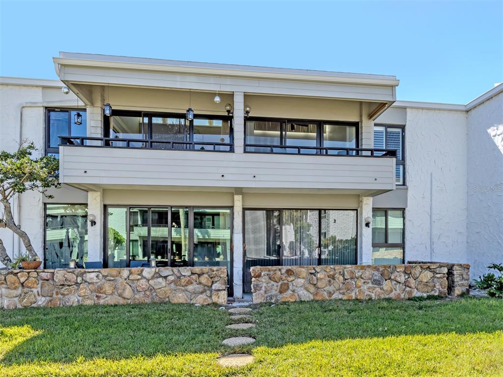 A two-story building exterior features a stone patio wall, sliding glass doors, and a balcony — 1555 TARPON CENTER DRIVE UNIT 242, VENICE, FL