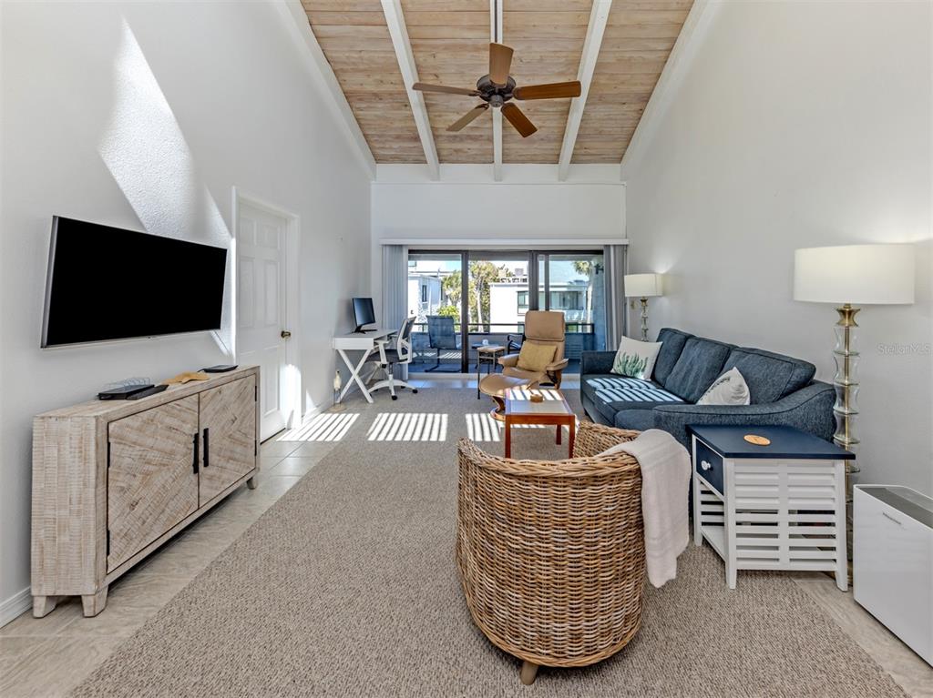 A living room features a vaulted wood-beam ceiling, a blue sofa, and a wicker chair — 1555 TARPON CENTER DRIVE UNIT 242, VENICE, FL