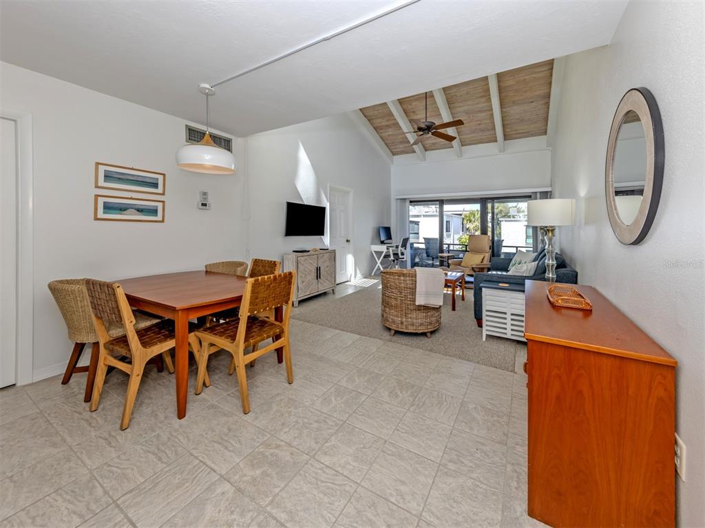 An open-concept living and dining area features vaulted wood-paneled ceilings, tile flooring, and sliding doors — 1555 TARPON CENTER DRIVE UNIT 242, VENICE, FL