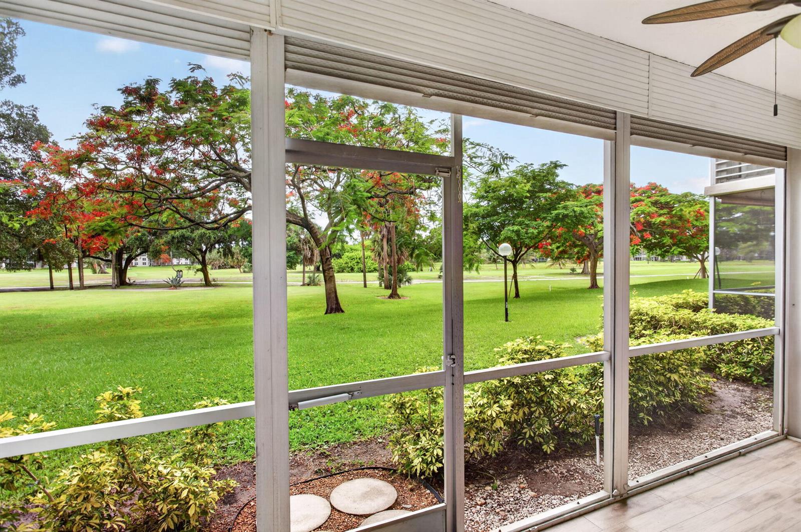 A screened-in porch overlooks a grassy lawn with flowering trees and a golf course — 3520 Oaks Way # 110, Pompano Beach FL 33069, POMPANO BEACH, FL