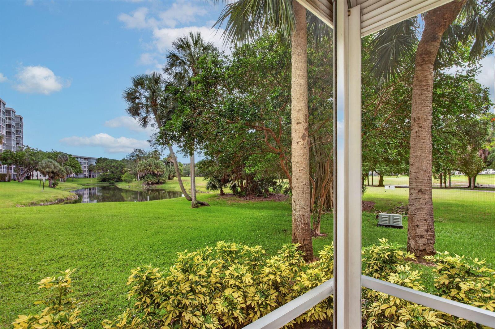 A view from a screened-in porch overlooking a grassy lawn, palm trees, and a pond — 3520 Oaks Way # 110, Pompano Beach FL 33069, POMPANO BEACH, FL