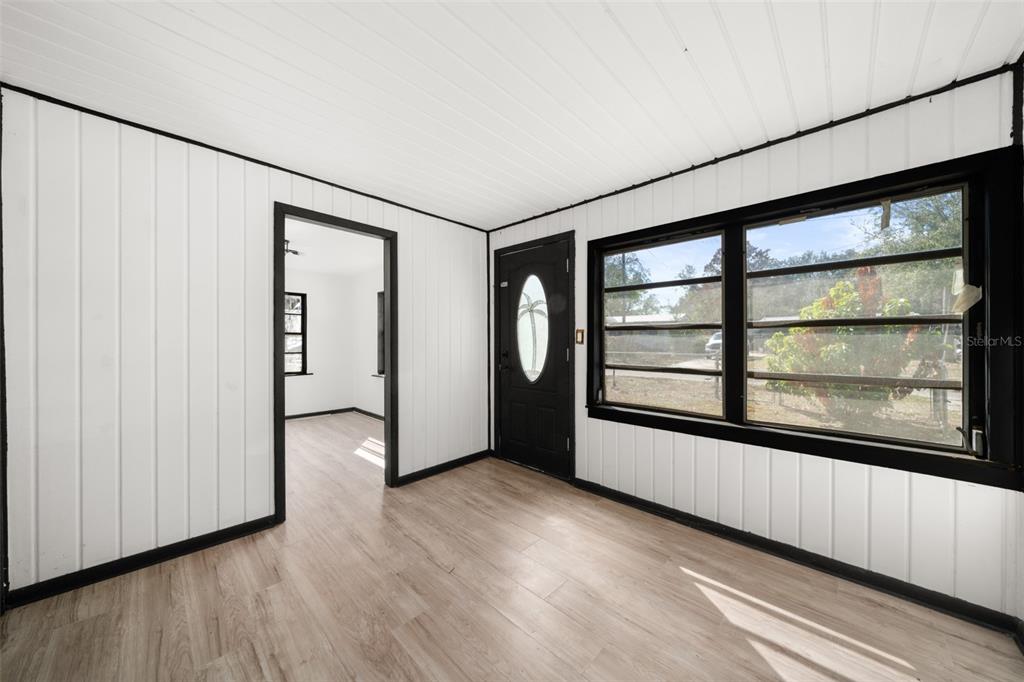 A room with white vertical paneling, black trim, light wood flooring, and a front door — 1628 WIGHTMAN AVENUE, SEBRING, FL