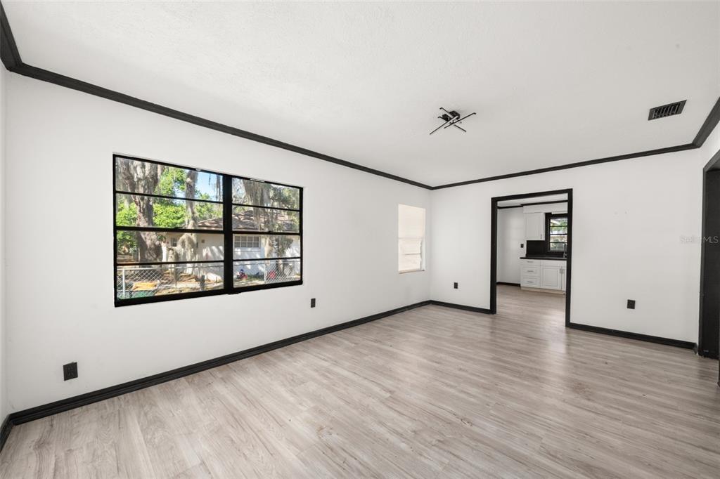 An empty living room with white walls, black trim, and light wood-look flooring — 1628 WIGHTMAN AVENUE, SEBRING, FL