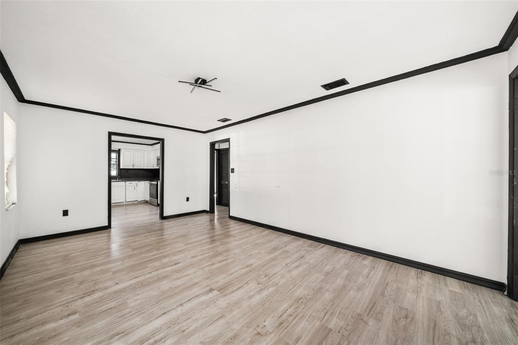 An empty room with white walls, black trim, and light wood-look flooring — 1628 WIGHTMAN AVENUE, SEBRING, FL