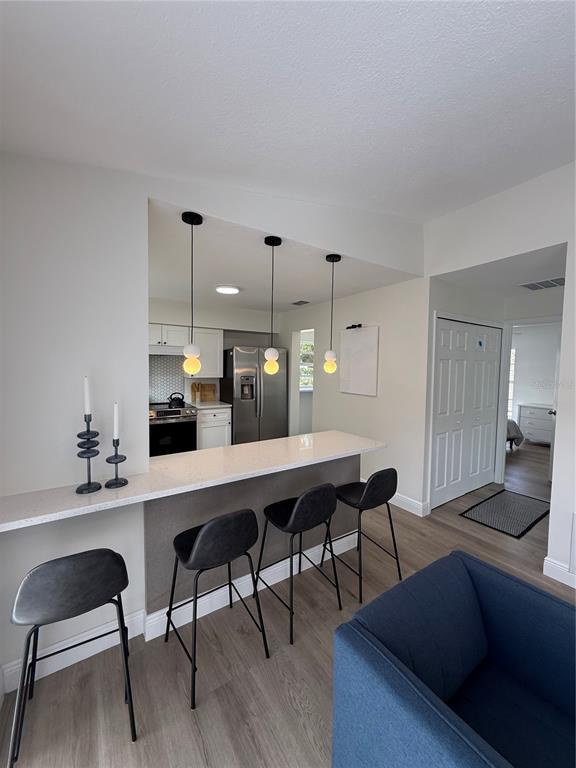 A kitchen with a breakfast bar, three pendant lights, and dark stools overlooks a living area — 2414 CENTER AVENUE, ORLANDO, FL