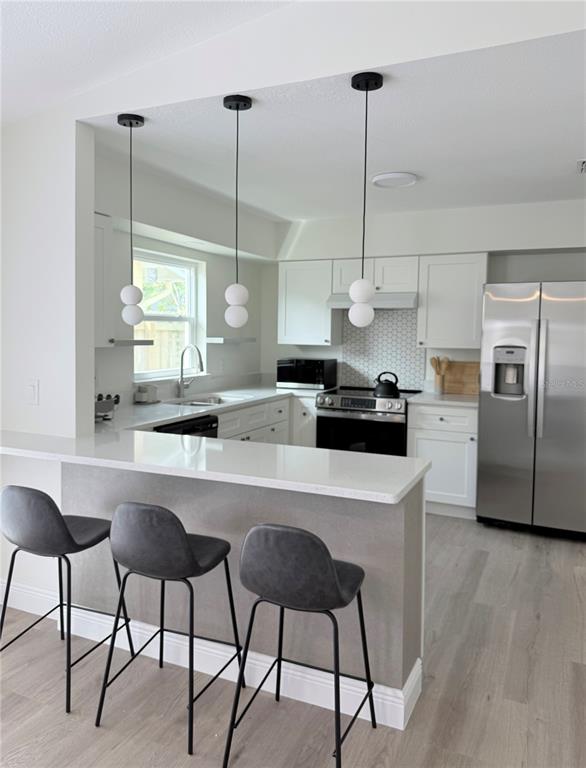 A kitchen features white cabinets, stainless steel appliances, a breakfast bar, and three pendant lights — 2414 CENTER AVENUE, ORLANDO, FL