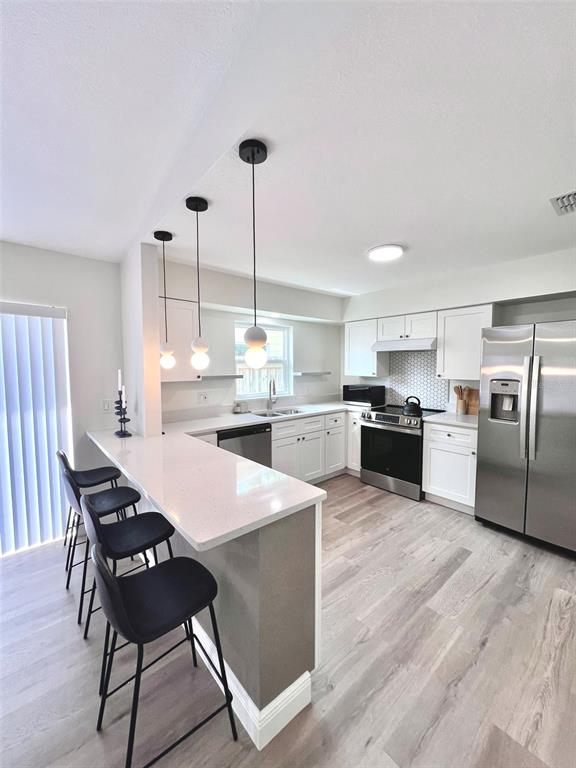 A modern kitchen features white cabinets, stainless steel appliances, and a breakfast bar with stools — 2414 CENTER AVENUE, ORLANDO, FL