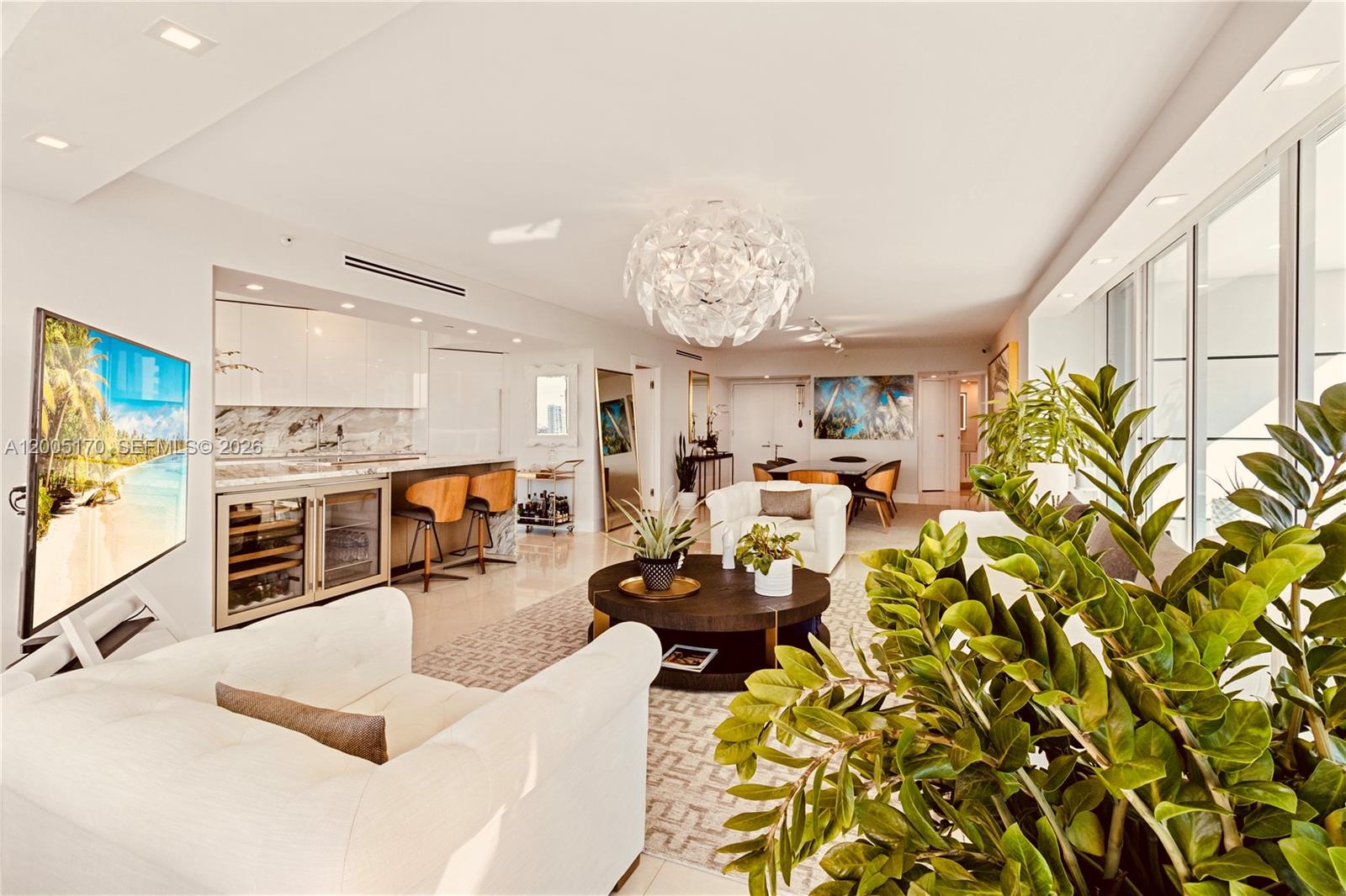 An open-concept living room and kitchen feature white cabinetry, a round coffee table, and plants — 2127 Brickell Ave # 1505, Miami FL 33129, MIAMI, FL