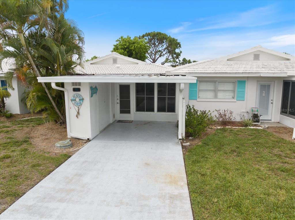 A white single-story house features a concrete driveway leading to a covered carport entrance — 702 FAIR WINDS DRIVE UNIT 702, NOKOMIS, FL