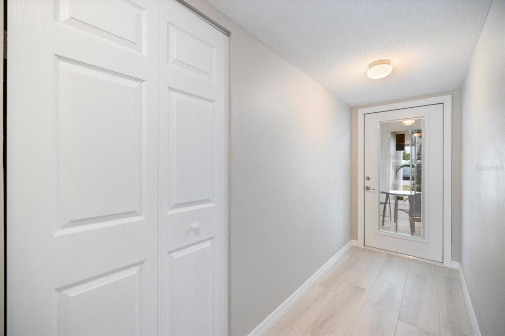 A hallway with light wood-look flooring, a white closet, and a glass-paneled exterior door — 702 FAIR WINDS DRIVE UNIT 702, NOKOMIS, FL