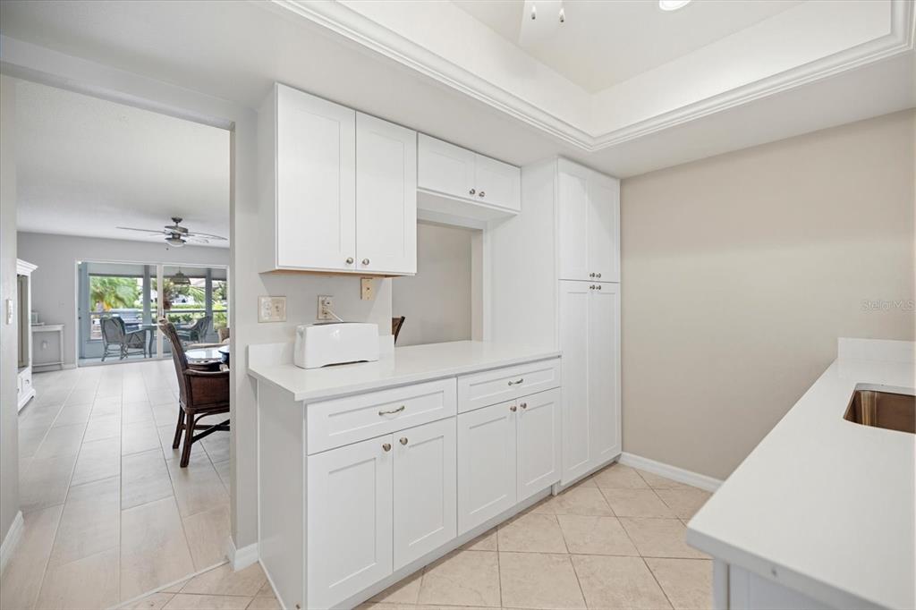 A kitchen features white cabinets, white countertops, and tile flooring, with a view into a sunroom — 702 FAIR WINDS DRIVE UNIT 702, NOKOMIS, FL